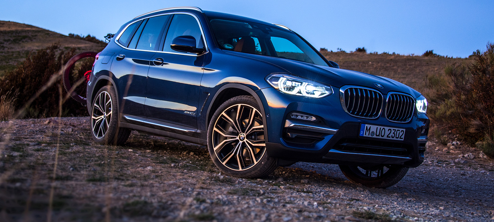Tummansininen BMW X3 maastossa Pysäköity tummansininen BMW X3, takateline ja maastopyörä maastossa