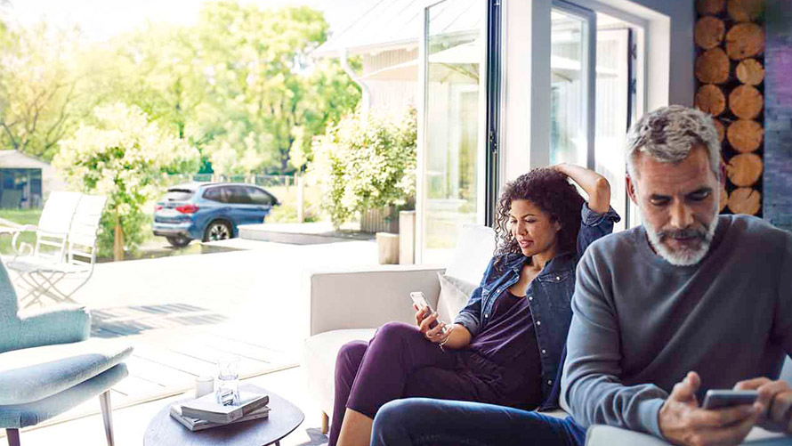 Remote Services -etätoiminnot Mies ja nainen istuvat sohvalla ja käyttävät Remote Services -etätoimintoja älypuhelimillaan