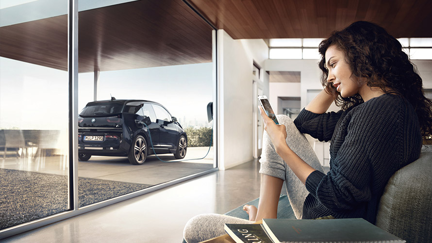 Digital Charging Service (ei saatavilla Suomessa) Nainen käyttää kotonaan älypuhelimella Digital Charging Service -toimintoa BMW i3 -autolleen