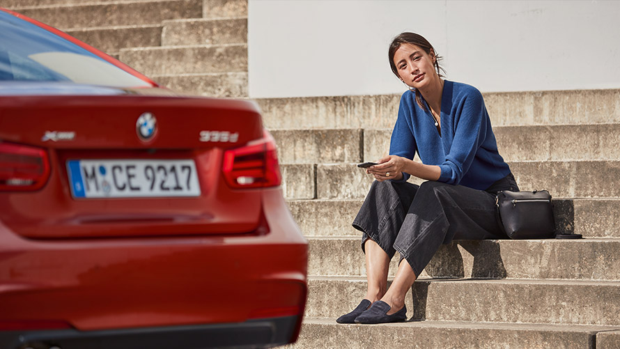 Huolto ja vikatilannepalvelu Nainen istuu punaisen BMW-autonsa edessä ja käyttää huolto- ja vikatilannepalvelutoimintoa