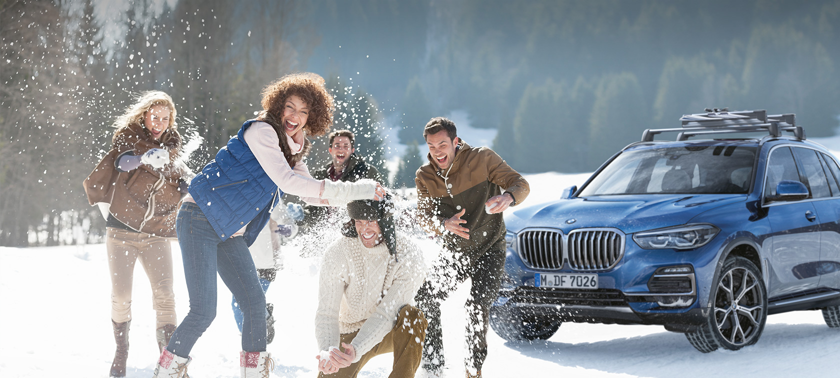 Alkuperäiset BMW-lisävarusteet ja BMW Services -palvelut syksyyn ja talveen Nauravia miehiä ja naisia lumessa BMWn edessä