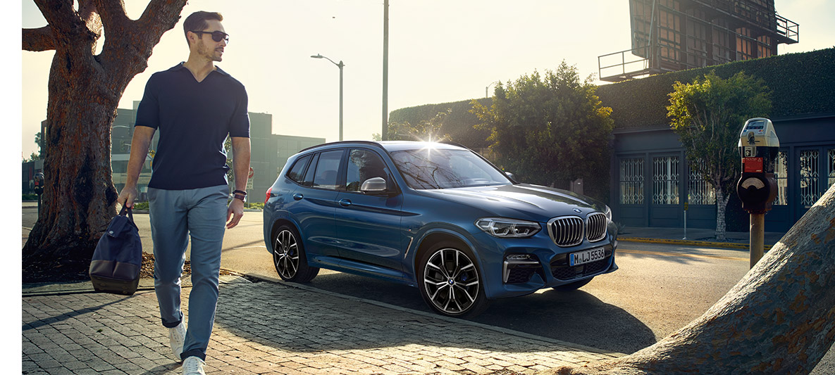 Mies aurinkolasit päässä sinisen BMW:n edessä Mies aurinkolasit päässä sinisen BMW:n edessä