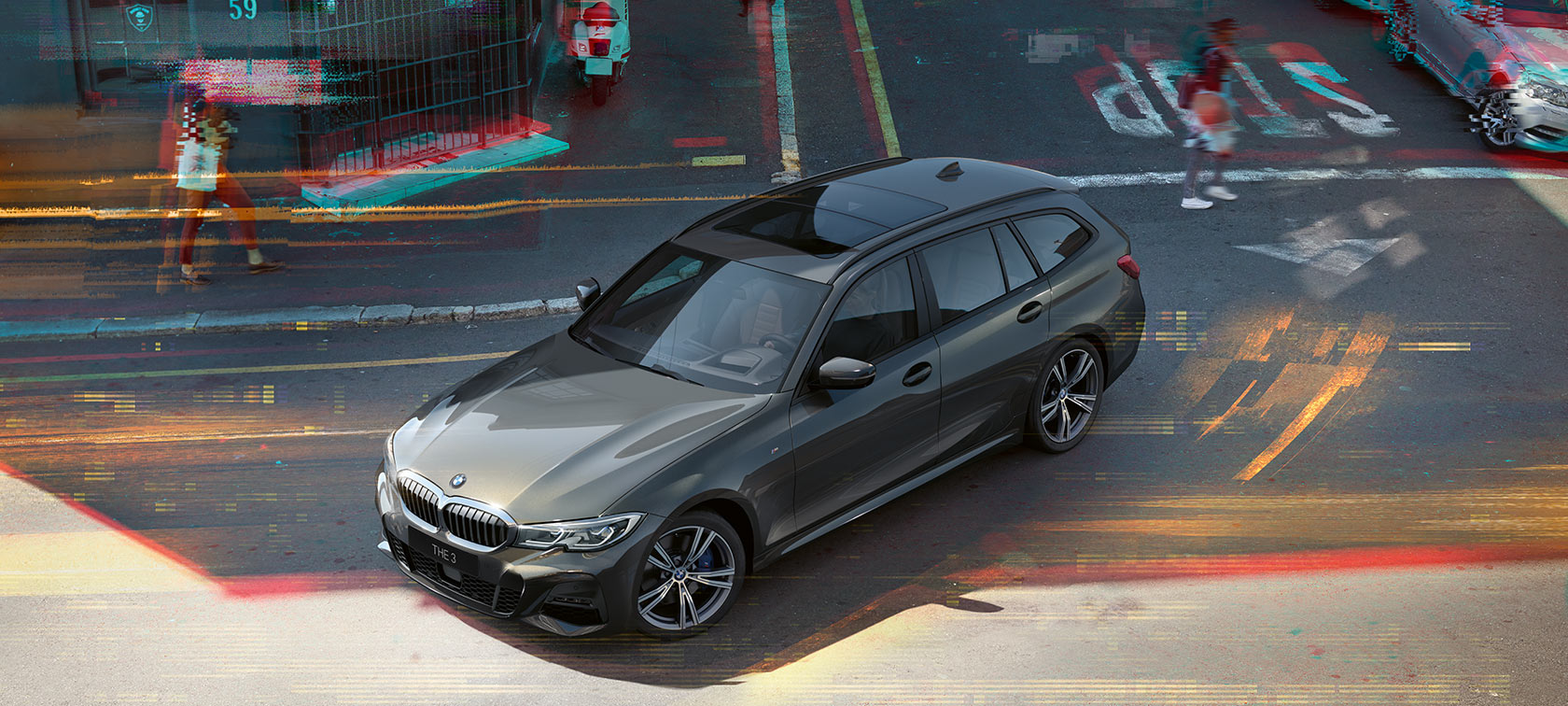 BMW 3-sarjan Touring, sivukuva talojen edessä ajavasta autosta, taustalla vuoria. 