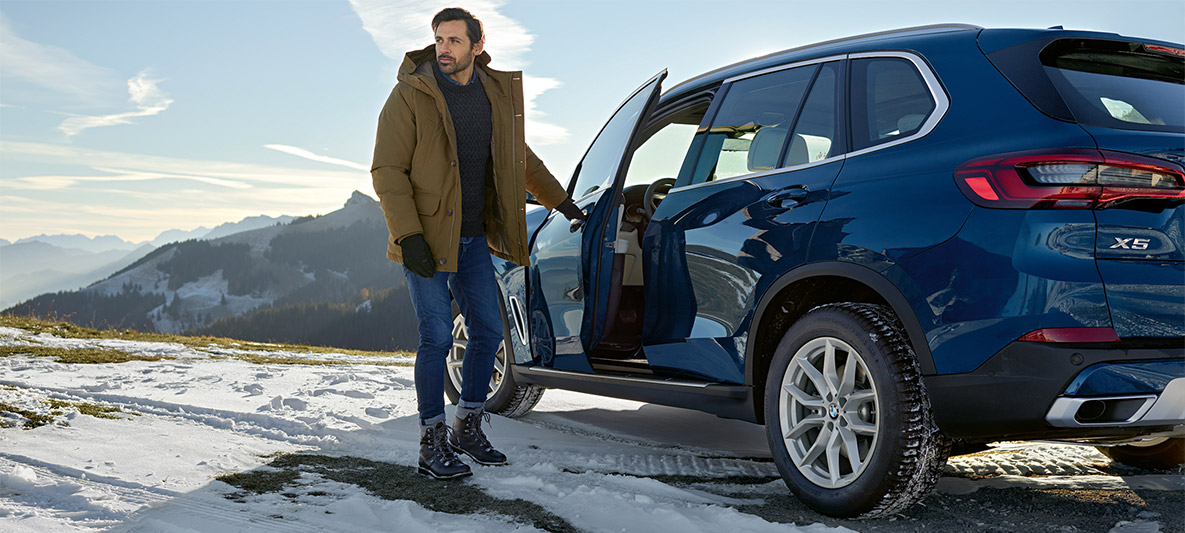 Mies aurinkolasit päässä sinisen BMW:n edessä Mies aurinkolasit päässä sinisen BMW:n edessä