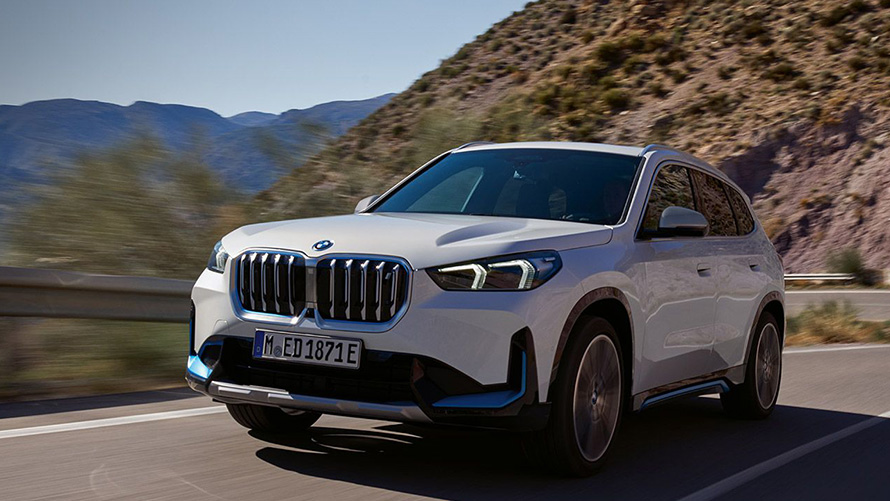 Vit BMW iX1 som kör på en landsväg. Vit BMW iX1 som kör på en landsväg.