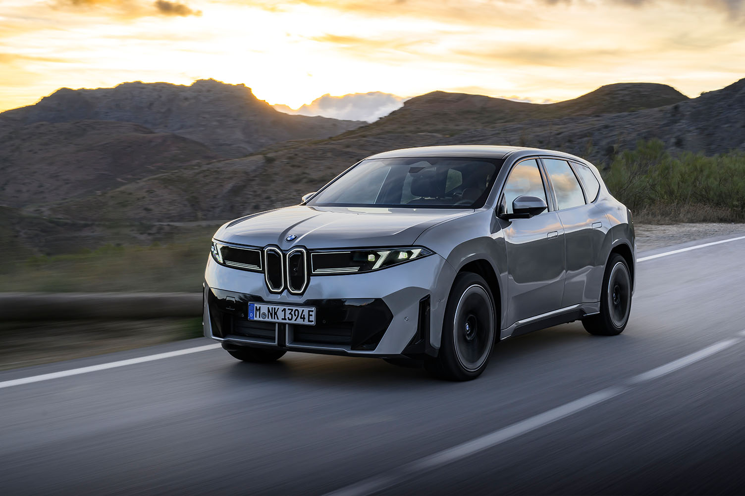 Harmaa BMW iX3, kuvattuna edestä viistosti auringonlaskun aikaan