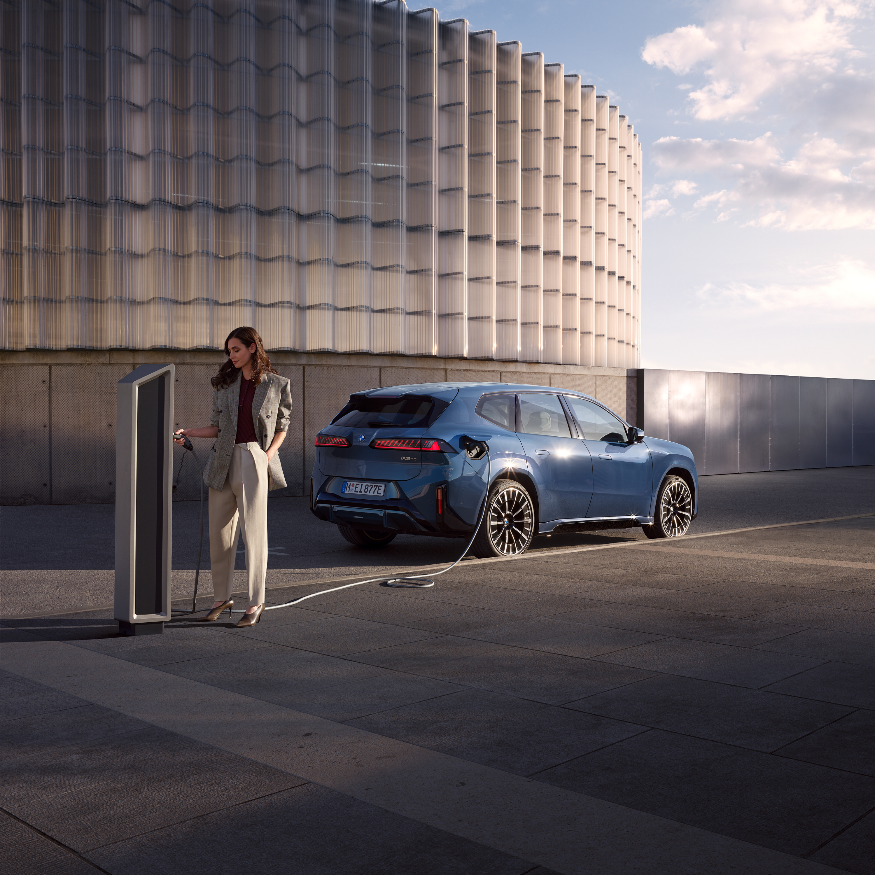 Mies seisoo BMW iX3:n vieressä, joka on yhteydessä julkiseen latausasemaan